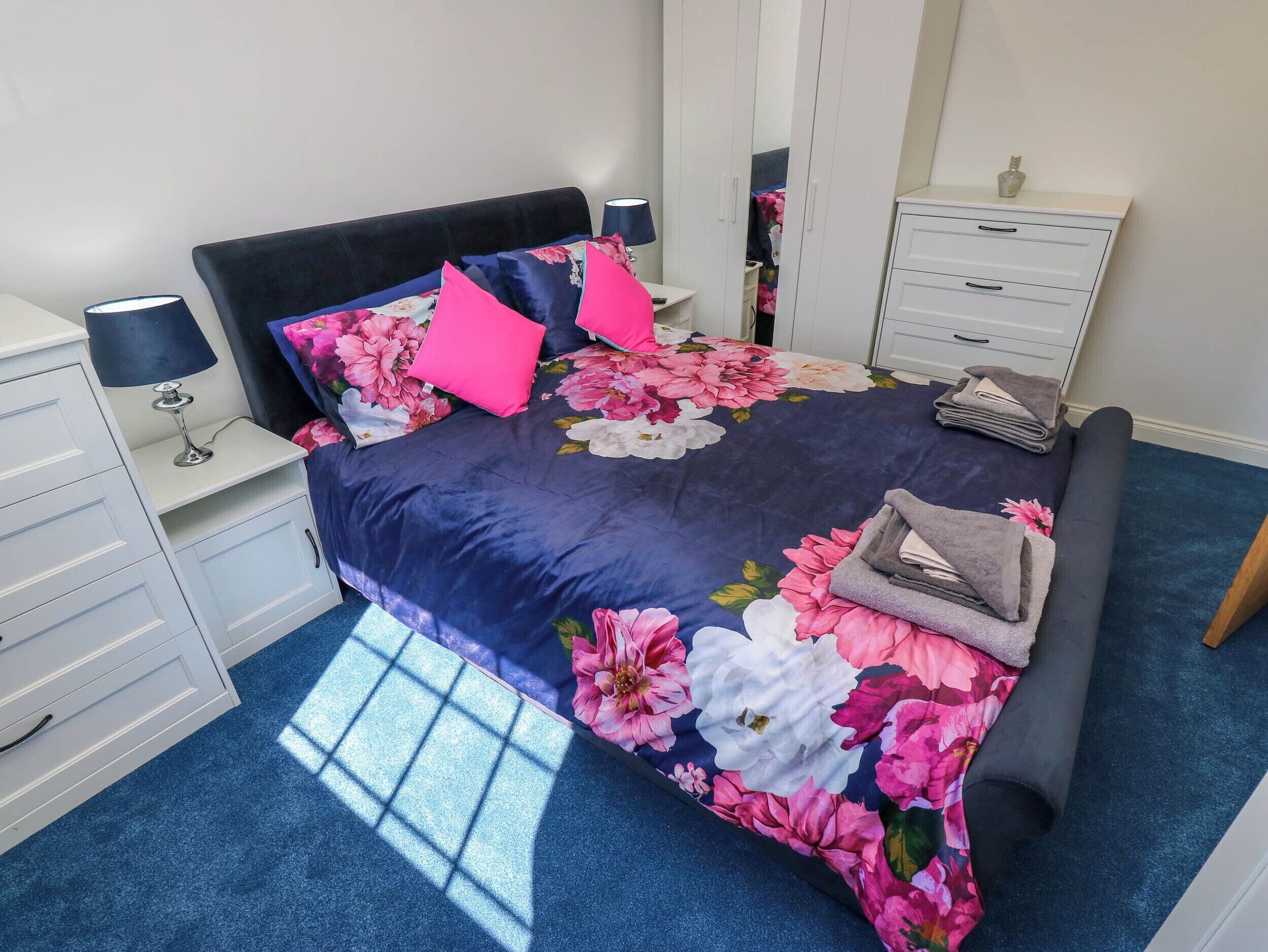 A bedroom with a bed, a nightstand, a dresser, and a mirror.