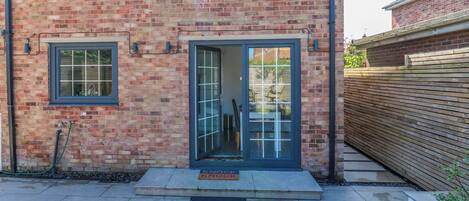 A brick building with a front door, a small window, and a wooden fence.