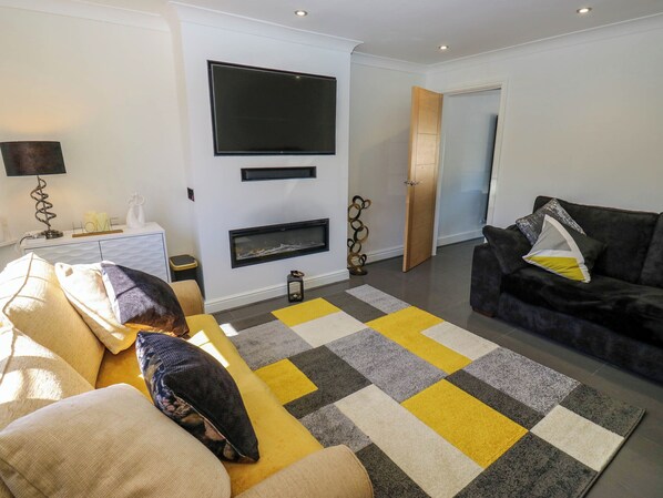 A modern living room with a sofa, a black leather couch, and a large TV mounted on the wall.