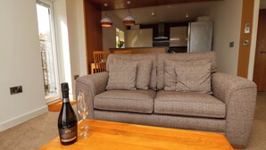 Een woonkamer met een beige bank, een houten salontafel en een fles wijn.