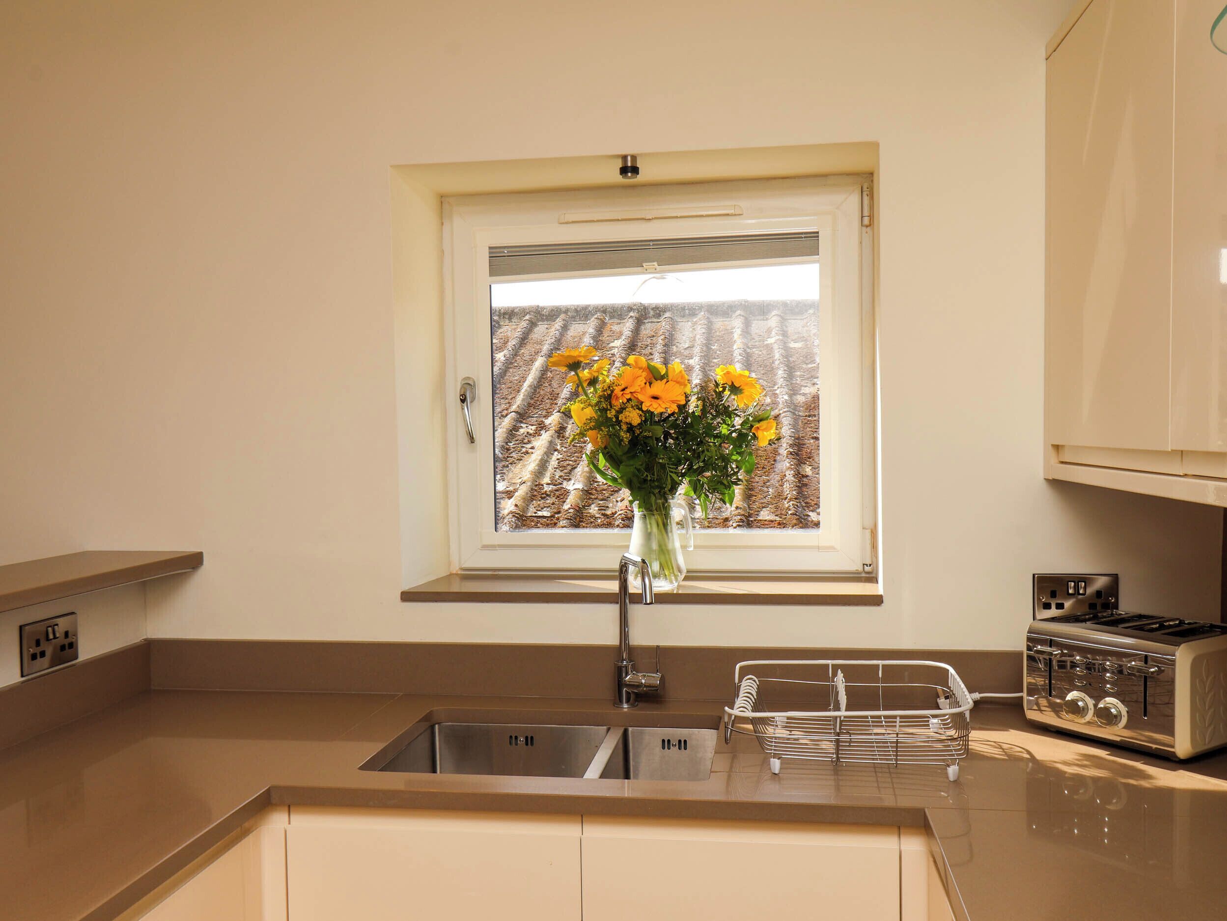 A kitchen with a window, a sink, a toaster, and a vase with flowers.