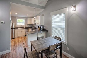 A modern kitchen with a central island, built-in appliances, and a dining area with a wooden table and chairs. - Historic Bungalow w/ Hot Tub, Walk to St. George (St. Augustine)