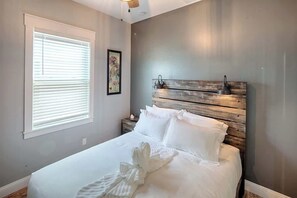 A neatly made bed with white linens and a pair of white bathrobes on it.
