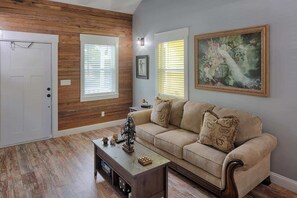Una sala de estar con un sofá color beige, paneles de madera en las paredes y un cuadro.