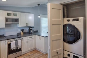 Une cuisine compacte avec des meubles blancs, un four à micro-ondes, un four traditionnel, ainsi qu’un lave-linge et un sèche-linge intégrés.