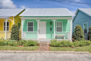 Un hilera de casas coloridas con una casa central verde que tiene una puerta y un porche blancos.