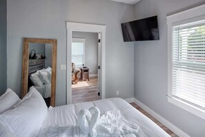 Ein Schlafzimmer mit einem großen Bett, einem flachbildfernseher an der Wand und einem Fenster mit Jalousien.