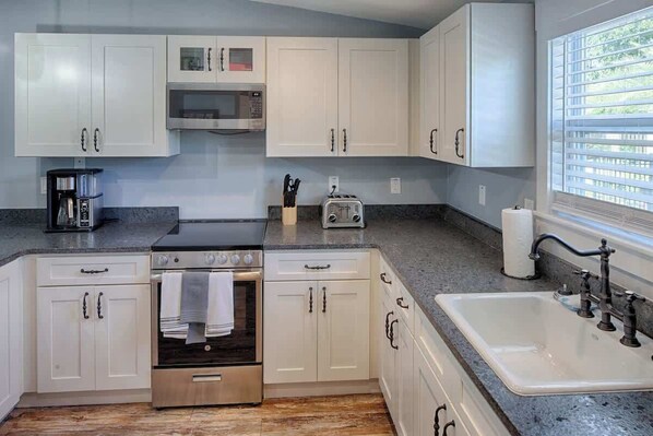 Una cocina con armarios blancos, un horno de acero inoxidable, un microondas, un tostador y un lavabo con grifo.