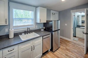 A modern kitchen with white cabinets, a stainless steel refrigerator, a sink, and a window with blinds. - Historic Bungalow w/ Hot Tub, Walk to St. George (St. Augustine)