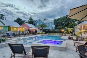 A swimming pool with lounge chairs and a hot tub, surrounded by colorful houses and a cloudy sky. - Historic Bungalow w/ Hot Tub, Walk to St. George (St. Augustine)