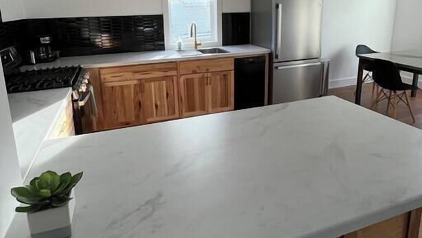 A modern kitchen with white countertops, wooden cabinets, a stainless steel refrigerator, and a hanging pendant light. - The Royal Union w/ king & queen bed (Calumet Township)