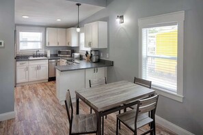 A modern kitchen with white cabinets, a wooden dining table, and a large window with blinds.