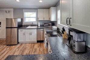 A modern kitchen with stainless steel appliances, white cabinetry, and a granite countertop.