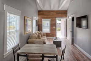 A dining area with a wooden table and chairs, a sofa, and a TV mounted on the wall. - Historic St. Augustine Bungalow: Walk to Sites & (St. Augustine)