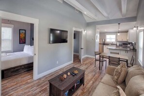 A modern apartment with a living room, dining area, and kitchen. There is a bed, a TV, and a dining table with chairs.