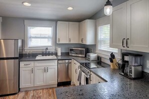 A modern kitchen with white cabinets, stainless steel appliances, a granite countertop, and a coffee maker.