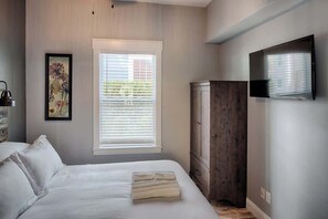 Un dormitorio con cama, ventana con persianas, armario y televisor de pantalla plana montado en la pared.