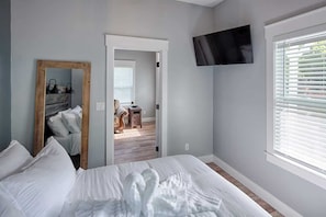 A bedroom with a bed, a TV mounted on the wall, and a window with blinds.