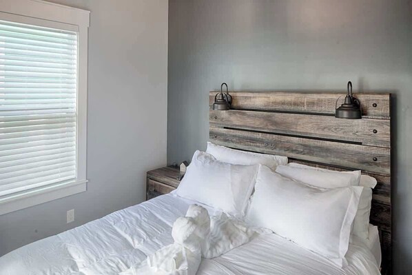A bedroom with a wooden headboard, white bedding, and a nightstand with a lamp.