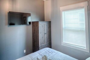 A bedroom with a bed, a wooden wardrobe, a mounted TV, and a window with blinds. - Historic St. Augustine Bungalow w/ Hot Tub & (St. Augustine)