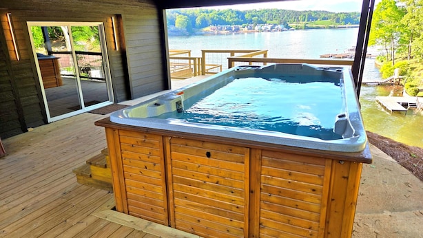 A wooden hot tub with a view of a lake and houses in the background.