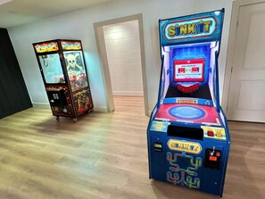 Two arcade machines, one labeled 'Sink It' and the other 'Pachy King', in a room with wooden flooring and white walls.