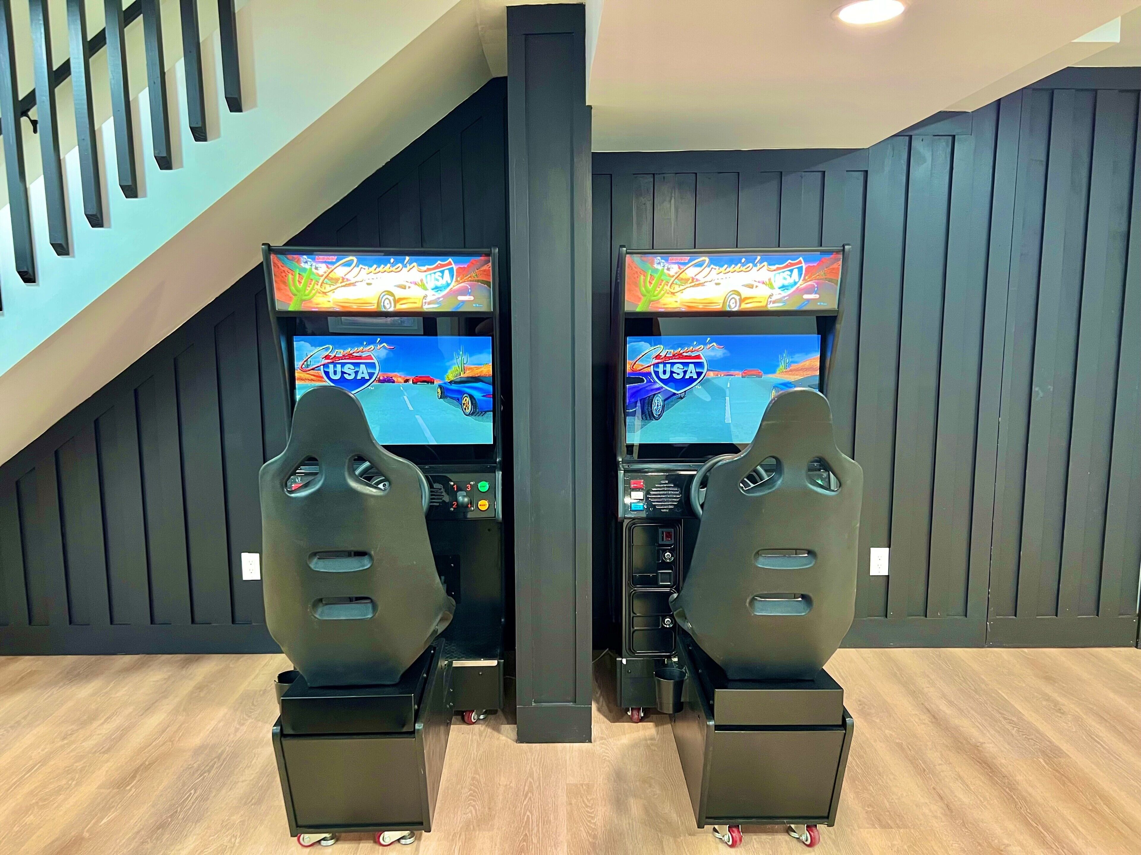 Twee racegames met sturen in een speelhal, voor een donkere houten wand met een trap aan de linkerkant.