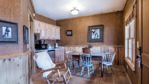 Una cocina rústica con armarios de madera, una mesa de comedor con cuatro sillas, un sillón mecedora y una lámpara de techo.