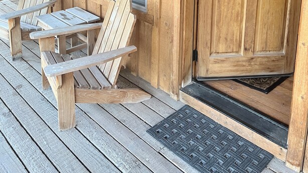 Una cabaña de madera con un porche, dos sillas Adirondack, una puerta con un número y una ventana.