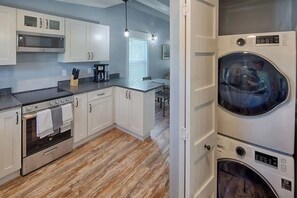 A modern kitchen with white cabinets, a stainless steel oven, a microwave, and a built-in washer and dryer.