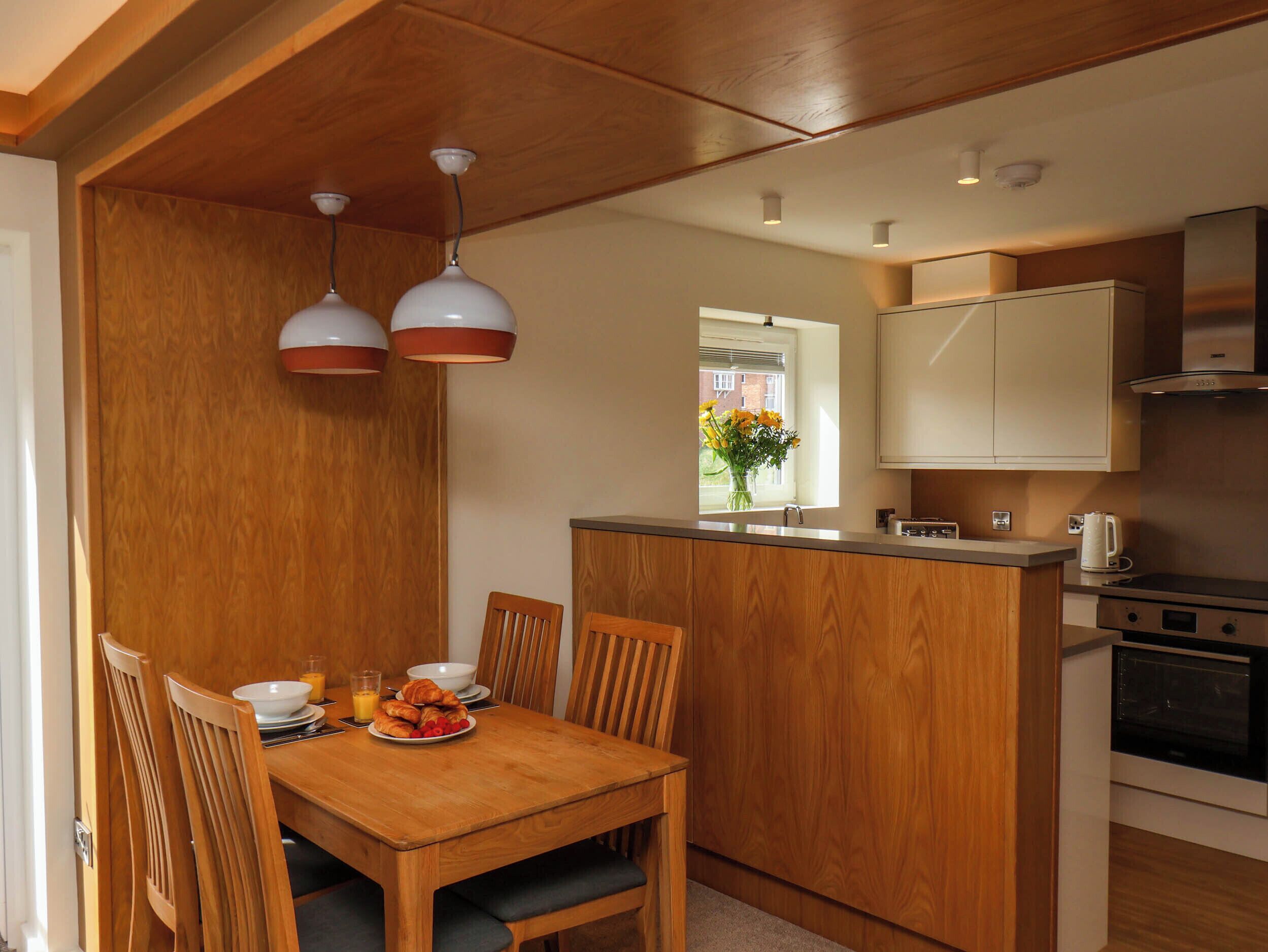 A modern kitchen with wooden cabinetry, a central island, and a dining area with a wooden table and chairs.