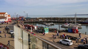 A marina with boats docked, a pier with people walking, and a road with cars and pedestrians. - Apartment 2 (Scarborough)