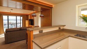 A modern kitchen with a central island, wooden ceiling beams, and a view of a marina through large windows. - Apartment 2 (Scarborough)