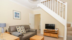 A living room with a sofa, coffee table, TV stand, and a staircase. - Malting Cottage (Dawlish)