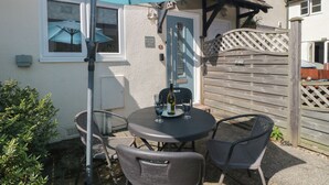 A patio with a table and chairs, a blue umbrella, and a house with a blue door and a sign reading "Malting Cottage No. 5". - Malting Cottage (Dawlish)