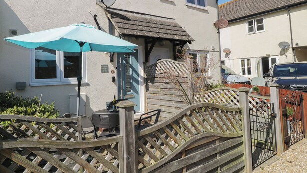 A cottage with a wooden gate, a patio with a table and chairs, and a satellite dish on the roof. - Malting Cottage (Dawlish)
