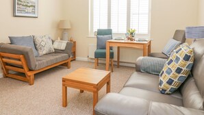 A cozy living room with a sofa, a chair, a coffee table, and a lamp. - Malting Cottage (Dawlish)
