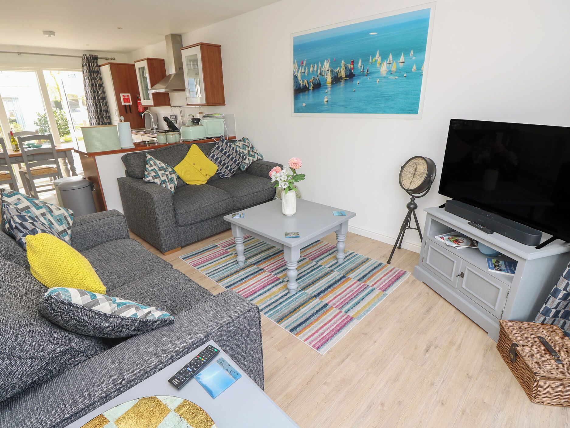 A living room with a grey sofa, a coffee table, a TV, and a painting of sailboats on the wall.