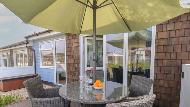 A patio with a glass table, wicker chairs, and a yellow umbrella.