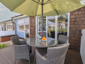 Eine Terrasse mit einem Glastisch, Korbstühlen und einem gelben Sonnenschirm.
