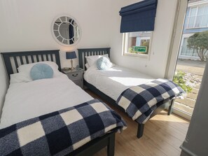 Ein Schlafzimmer mit zwei Betten, einem Nachttisch mit Lampe, einem Spiegel und einem Fenster mit einem Notausgangsschild.