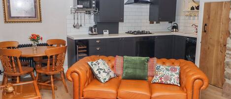 A compact living space with a kitchenette, a dining area with a round table and chairs, and a sofa with decorative pillows.