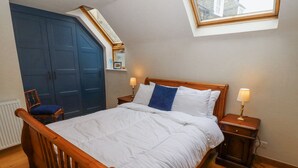 Une chambre avec un lit en bois, deux tables de chevet avec des lampes, une chaise bleue, une grande porte bleue et une lucarne.