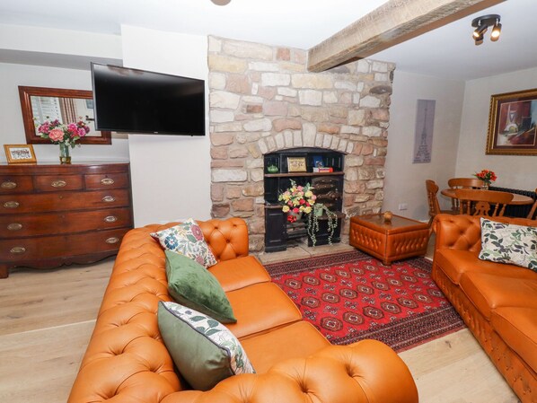 A living room with a stone fireplace, leather sofas, a wooden coffee table, and a flat-screen TV mounted on the wall. - Muffins (Wooler)