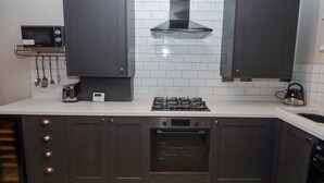 Une cuisine moderne avec des meubles de rangement de couleur sombre, une cuisinière à gaz, un four, un four à micro-ondes et une bouilloire.