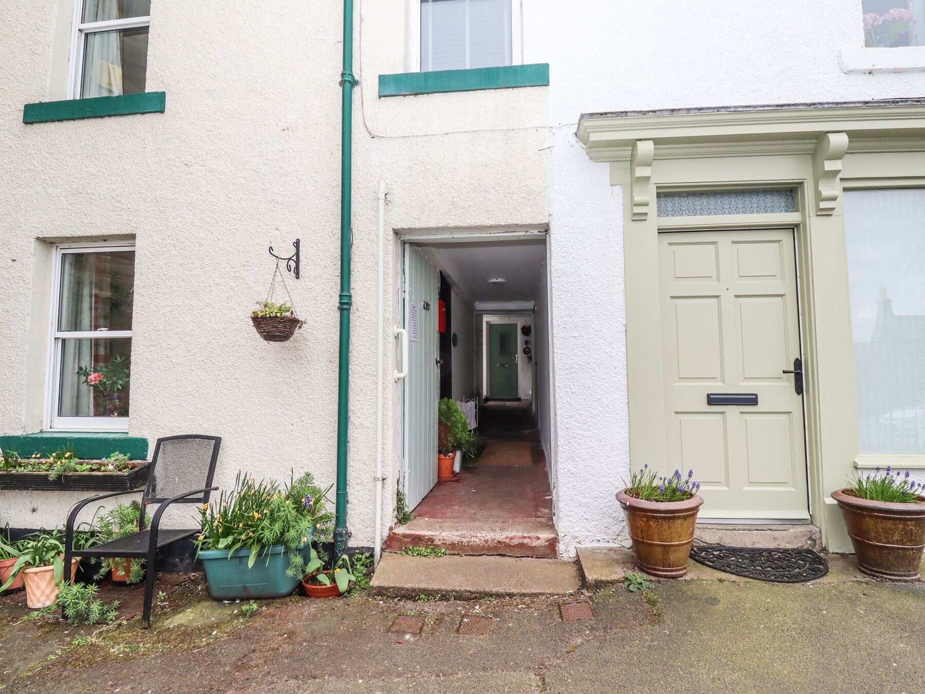 A narrow hallway leading to a door, with potted plants and a chair outside.