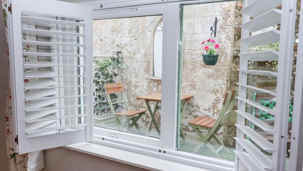 Une pièce dotée d’une grande fenêtre, d’un radiateur et donnant sur un espace extérieur aménagé avec une table et des chaises.