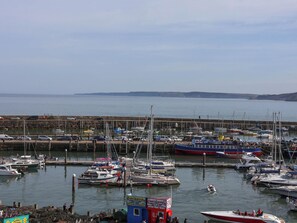 A marina with various boats docked, a small building with a sign, and a distant shoreline. - Apartment 3 (Scarborough)