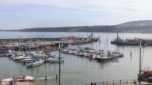 A marina with various boats docked, a lighthouse in the background, and a hilly landscape across the water. - Apartment 3 (Scarborough)