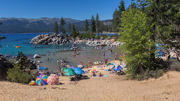 A beach with clear water, rocks, and people.